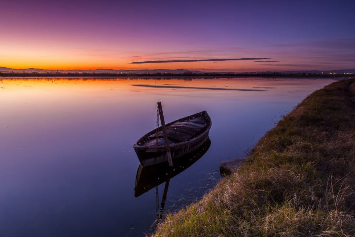 An Old Boat Stands In The Water At Sunset