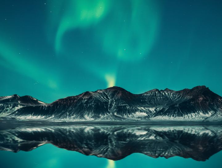 Green Aurora Borealis In The Sky Above The Mountains By The Lake